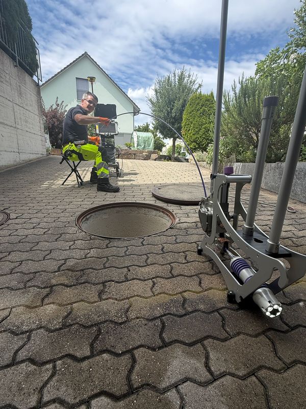 Beleuchteter Kamerakopf im Führungsgerät am Schacht, im Hintergrund steuert ein Greentech-Techniker die Kamerafahrt am Monitor